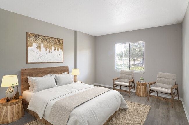 Bedroom with bed, two chairs by a window, neutral tones, and art.