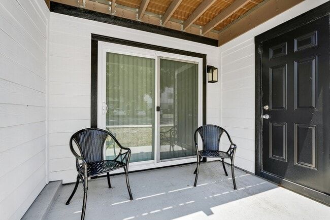 Two black chairs on a patio, near a sliding glass door and a black door.