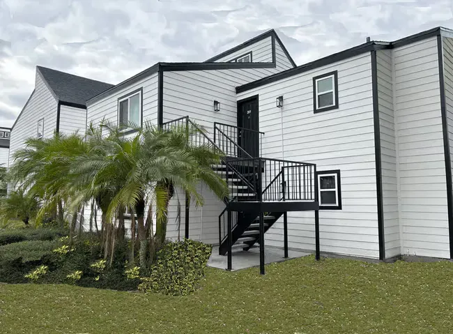 Two-story white apartment building with black trim and exterior stairs. Palm trees and grass in front at The Retreat at Altamonte Springs