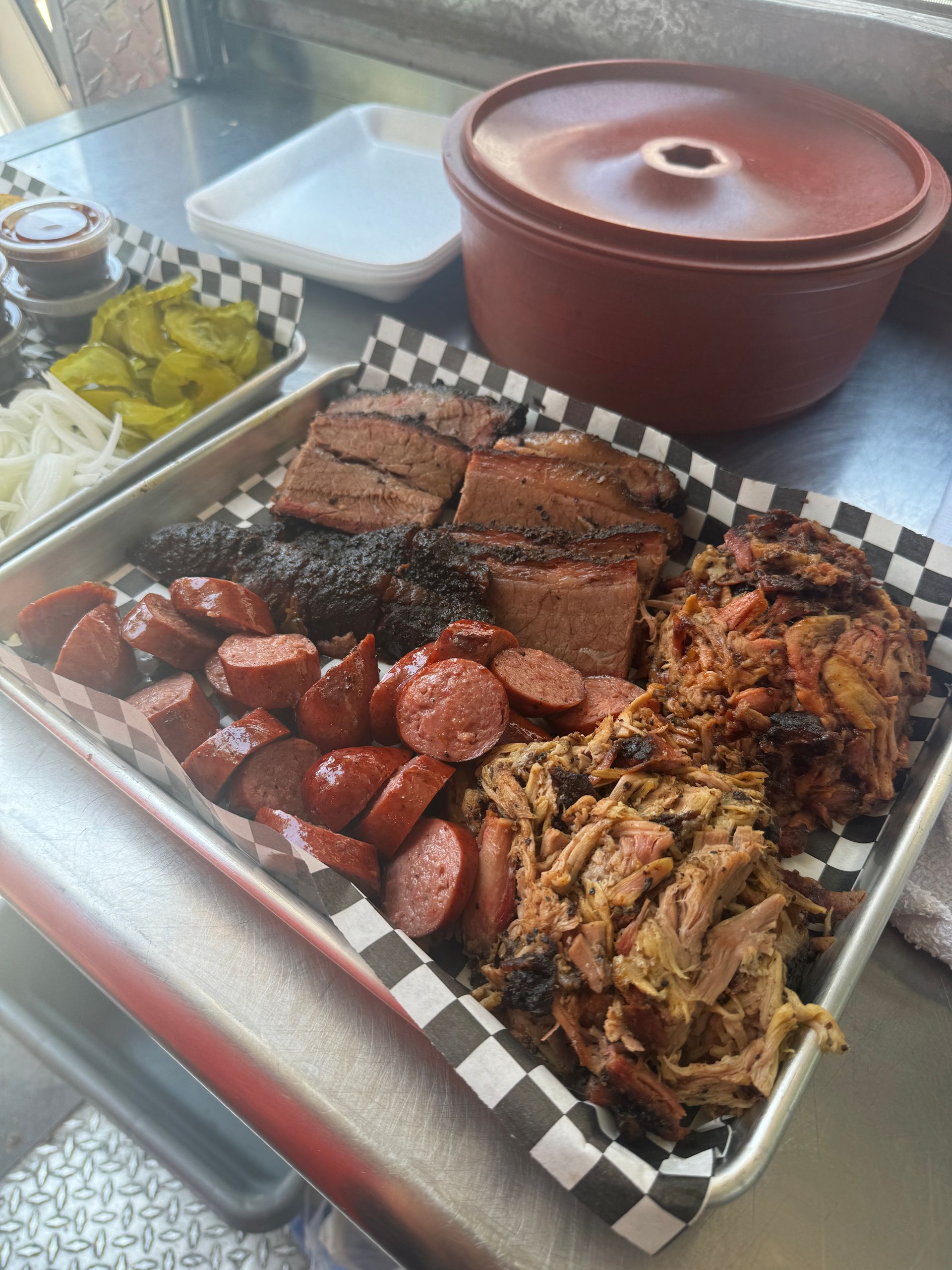 A tray of meat and sausage on a checkered paper on a table.