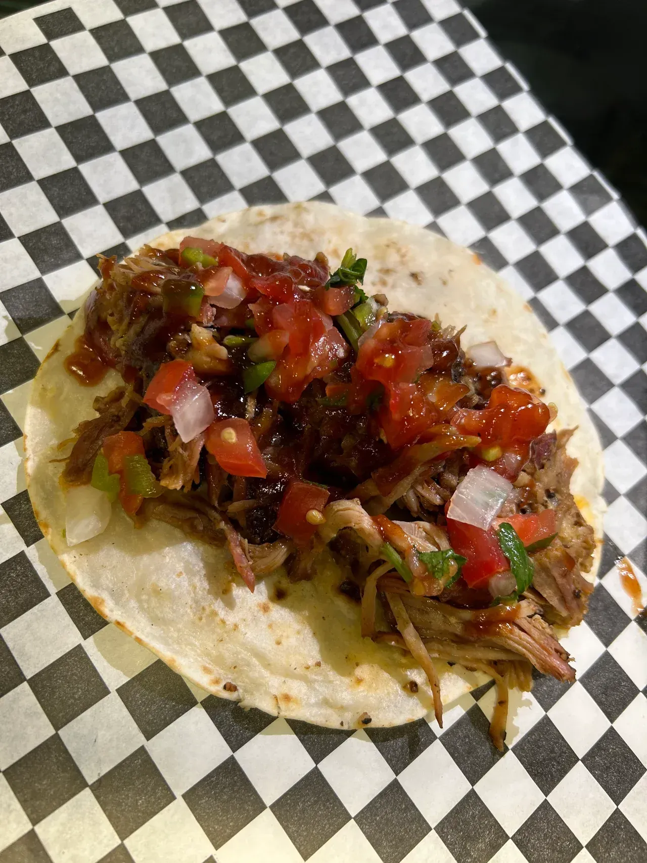 A taco with meat and salsa is sitting on a checkered paper.