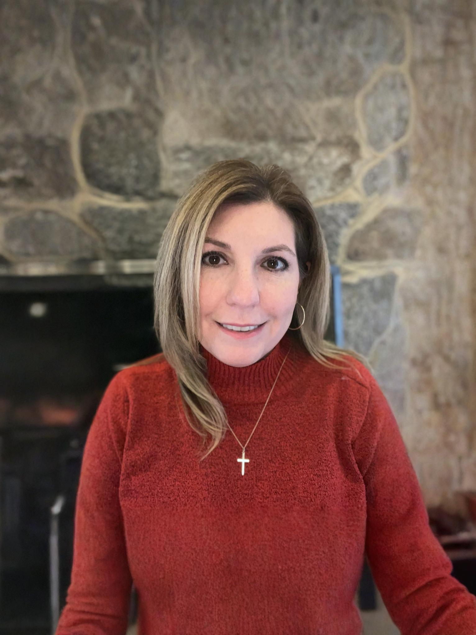 Woman with blonde highlights smiling, wearing a rust-colored sweater.