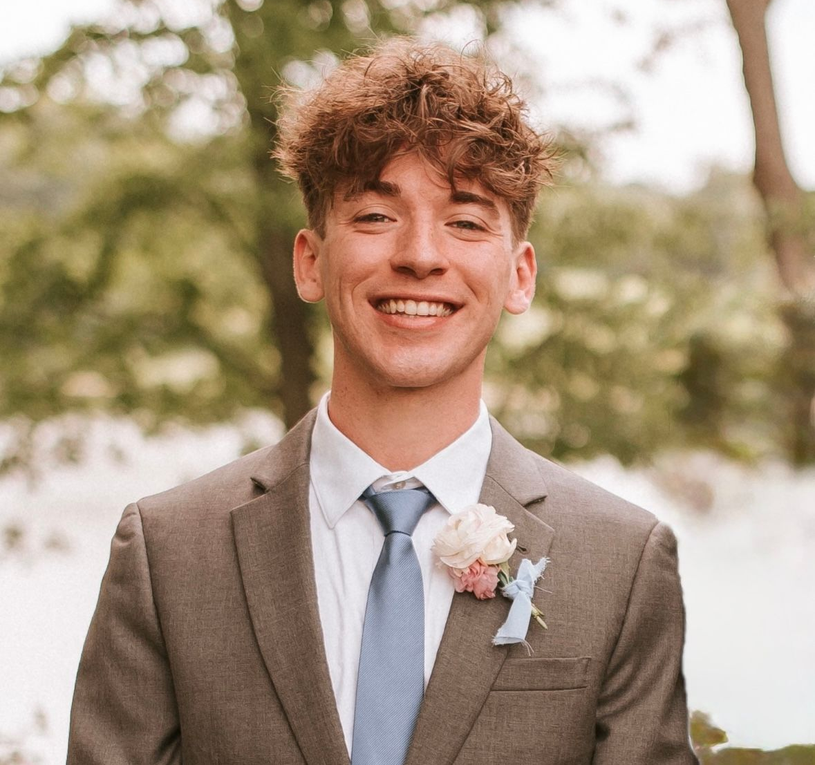 Woman with blonde highlights smiling, wearing a rust-colored sweater.