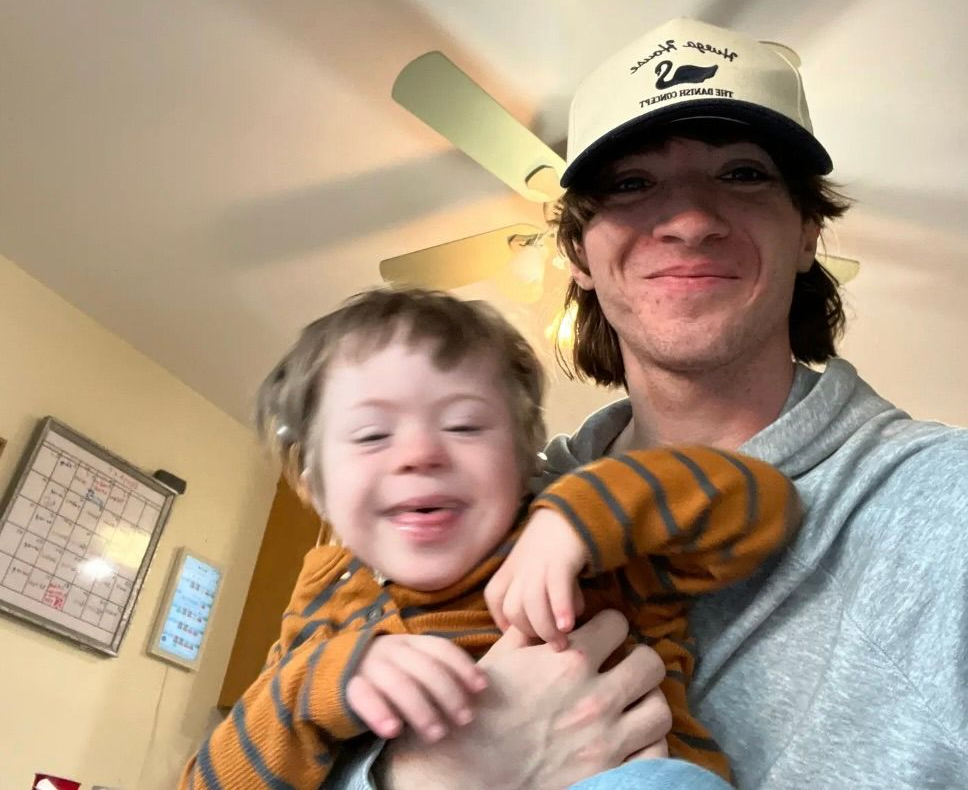 Woman with short brown hair smiles, wearing a navy top, against a dark blue background.