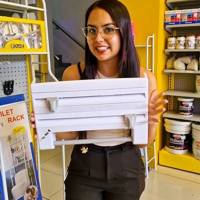 Mujer con gafas sonriendo, sosteniendo un organizador de cocina blanco en una tienda muy iluminada.