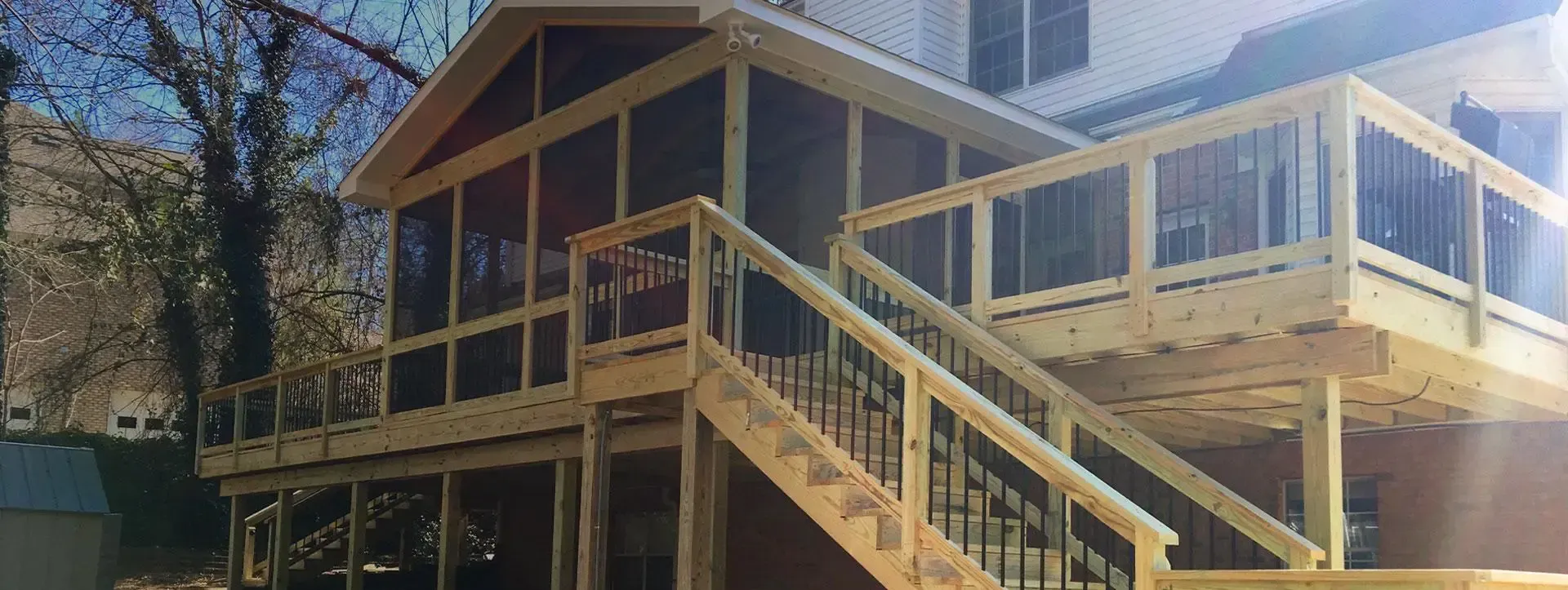 A multi-level wooden deck with a screened-in porch, staircase, and glass railings attached to the side of a house.