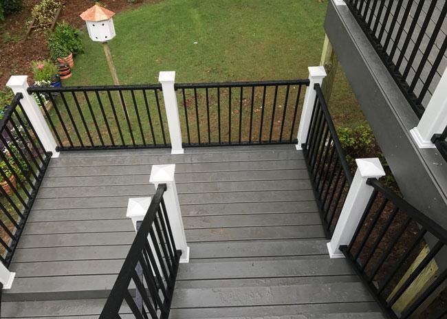 A gray deck with black metal railings and white posts, overlooking a grassy yard with a small birdhouse.