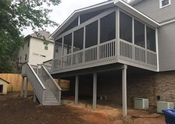 A gray wooden screened-in porch with a staircase attached to the back of a house with a stone foundation.