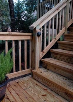 Wooden staircase with railing on an outdoor deck, featuring a small round light attached to the center post.