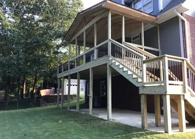 A wooden, elevated deck with a covered roof, stairs, and railings extending from the rear of a multi-story house.