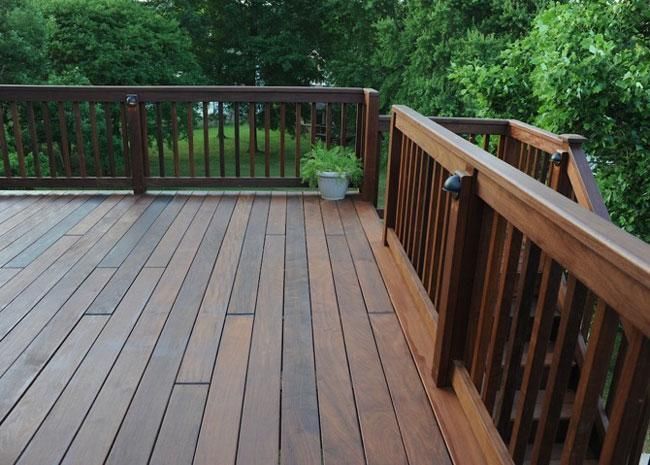 A wooden deck with railings overlooking a lush green yard, featuring a small potted plant in the corner.