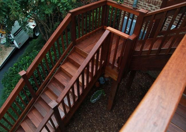 A high-angle view of a set of wooden outdoor stairs with railings, leading down to a mulched ground area.