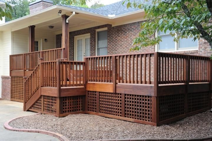 A raised brown wooden deck with lattice skirting and stairs, attached to a brick house exterior.