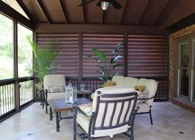 Covered patio with beige furniture, a coffee table, and potted plants in front of dark horizontal privacy screens.