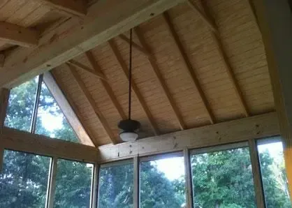 A screened-in porch with light wood beams, a vaulted tongue-and-groove ceiling, and a hanging ceiling fan.