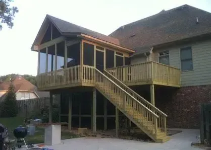 A two-story wood deck with a screened-in porch on the upper level and a staircase leading to a concrete patio.