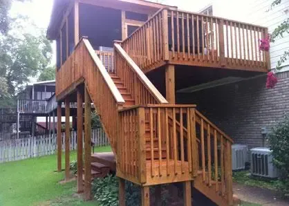 A wooden deck with a screened-in porch and stairs leading down to a backyard in a residential setting.