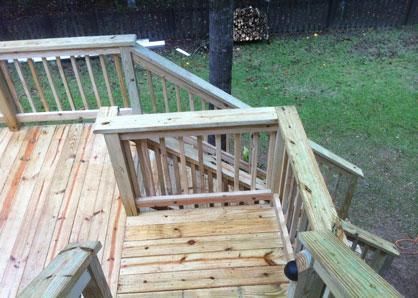A high-angle view of a new wooden deck with railings and stairs leading down to a grassy backyard.