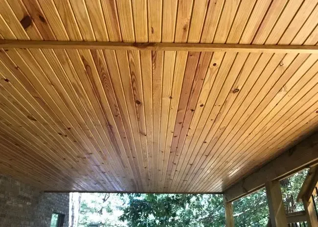 A view of a wooden ceiling with parallel planks and a horizontal support beam, seen from a covered outdoor patio.