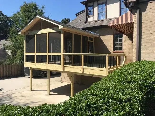 A new wooden deck with a screened-in porch addition attached to the side of a brick house.