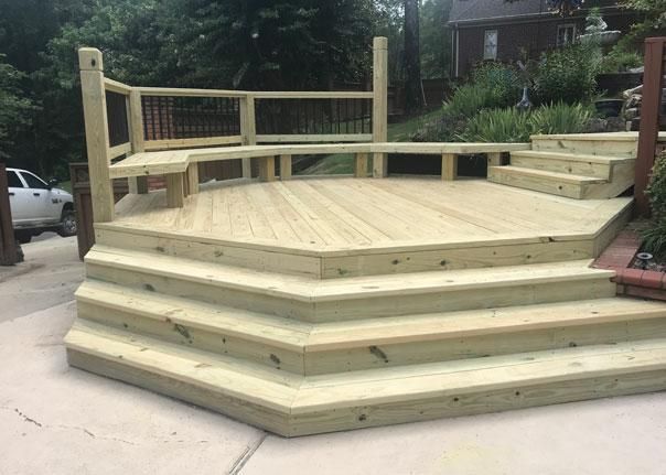 A newly built, multi-level wooden deck featuring curved bench seating and wide, wrap-around stairs on a concrete patio.