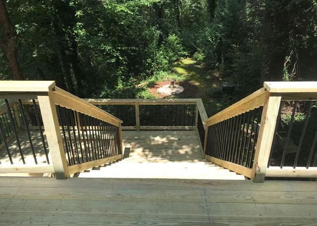 A wooden deck with a staircase leading down to a wooded yard with a circular stone fire pit area.