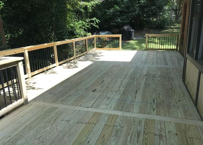 A wooden deck with railing extending out toward a backyard filled with trees and foliage.