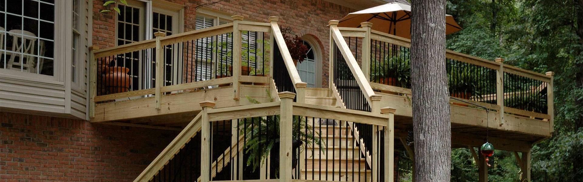 A raised wooden deck with a staircase, attached to a brick house and surrounded by trees.
