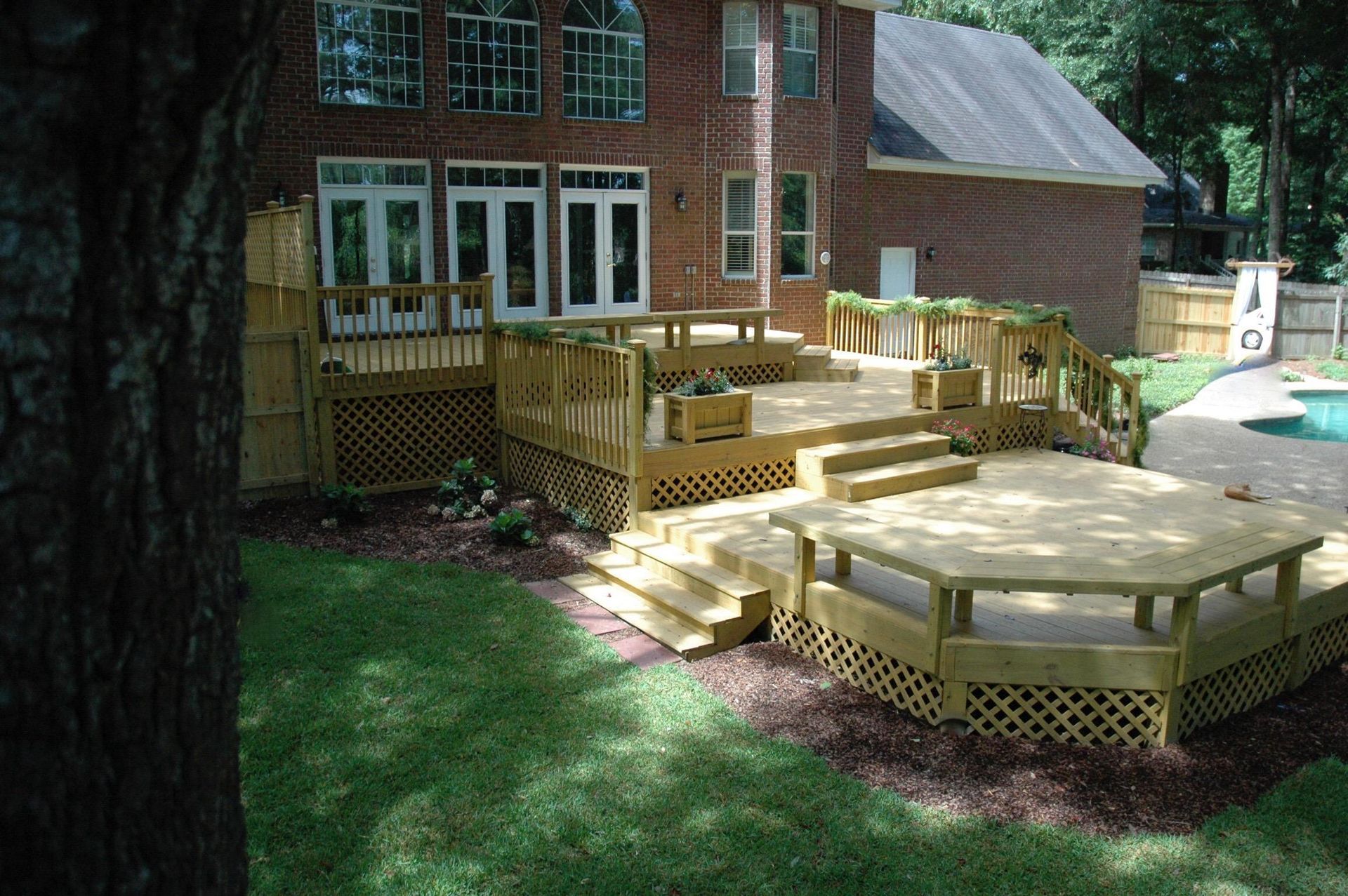 Multi-level wooden deck with built-in bench seating and lattice skirting attached to the rear of a brick house.