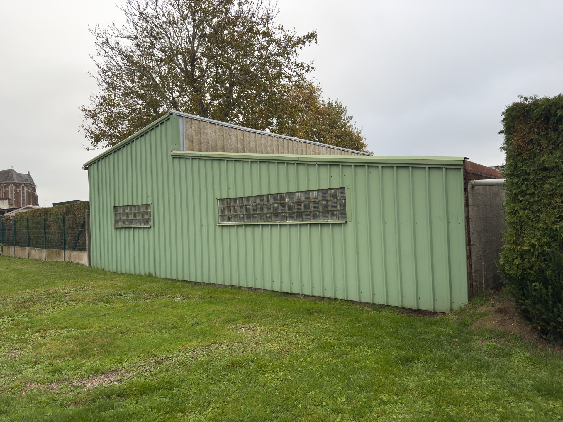 A green utility shed is on a grassy lawn.