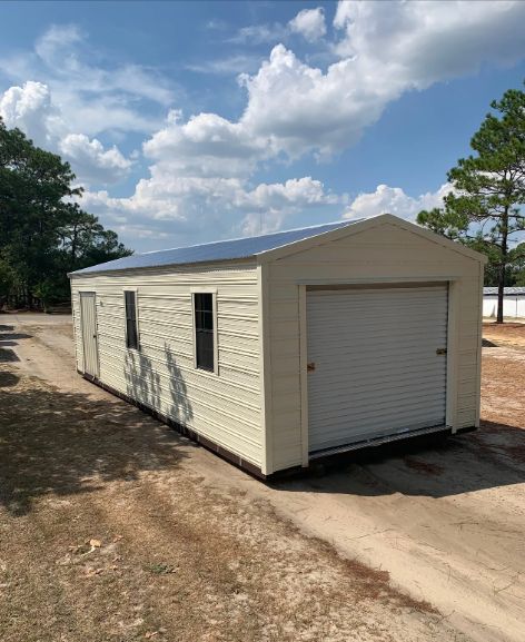 Tan metal garage with a roll-up door, side door, and two windows, on a gravel driveway under a partly cloudy sky.
