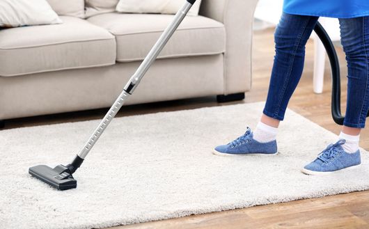 A woman is using a vacuum cleaner to clean a rug in a living room.