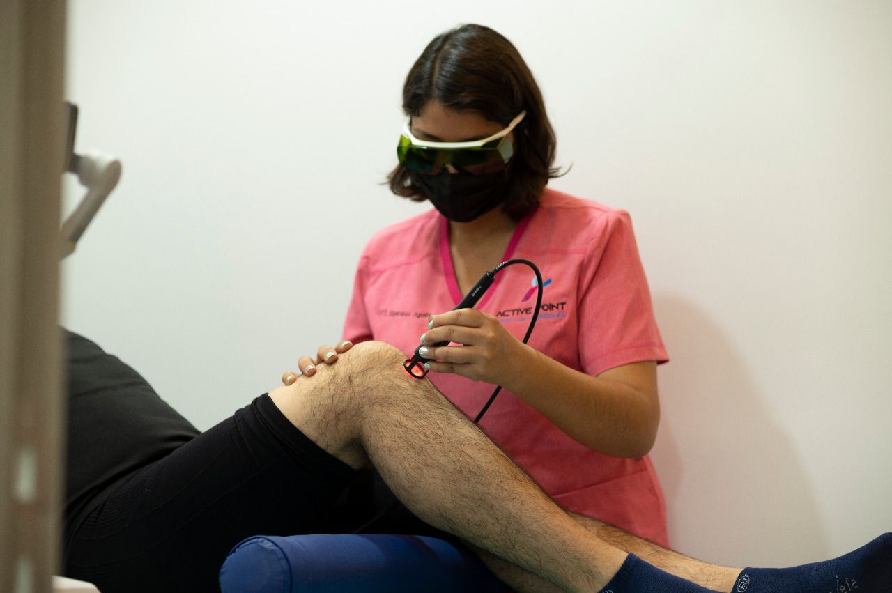 Persona que utiliza un láser en la rodilla de un paciente en un entorno médico.