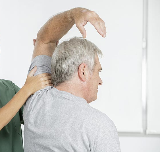 Woman in scrubs assisting a person with stretching their leg on a therapy table.