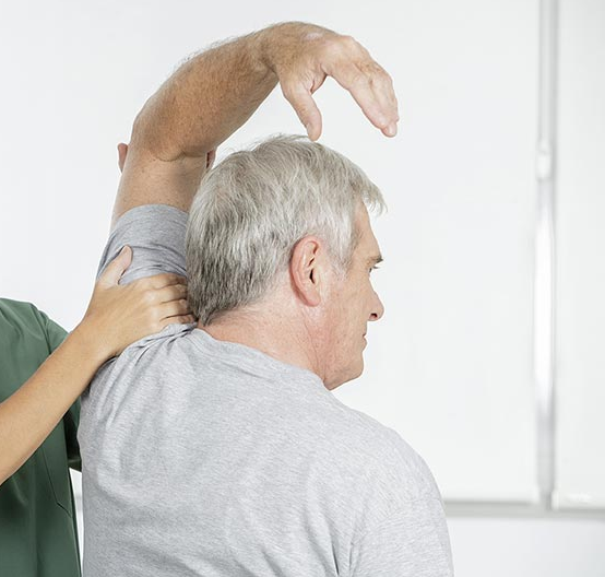 Fisioterapeuta ayudando a una persona a estirar el brazo en un entorno médico.