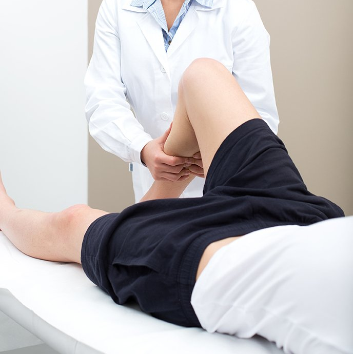 A una persona acostada en una mesa médica un médico con bata blanca le examina la pierna.