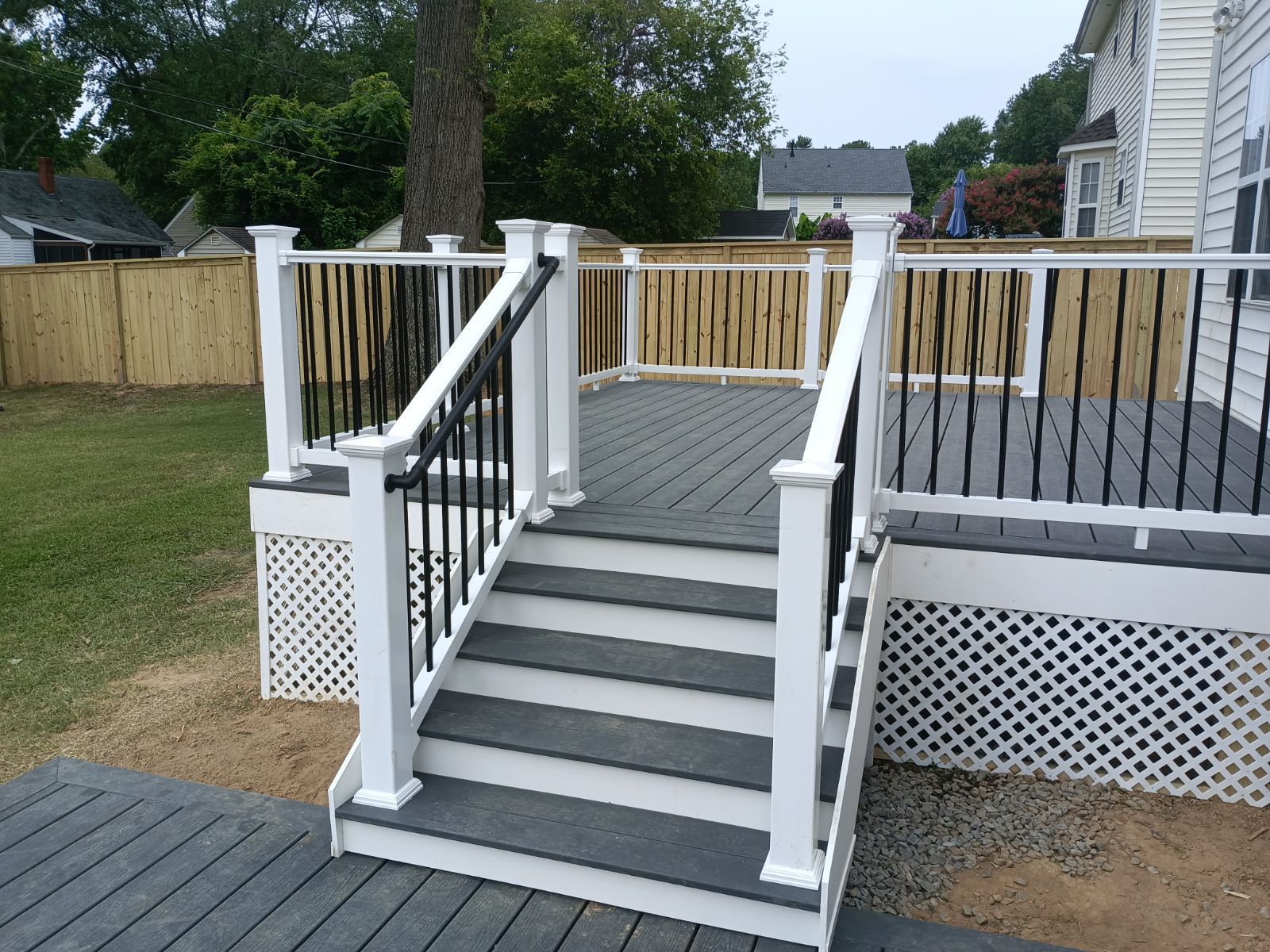 A gray and white deck with stairs, black railings, and a fenced yard.