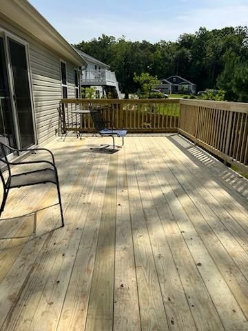 Wooden deck with railings and a small table, next to a house with sliding glass doors, overlooking a grassy area and trees.
