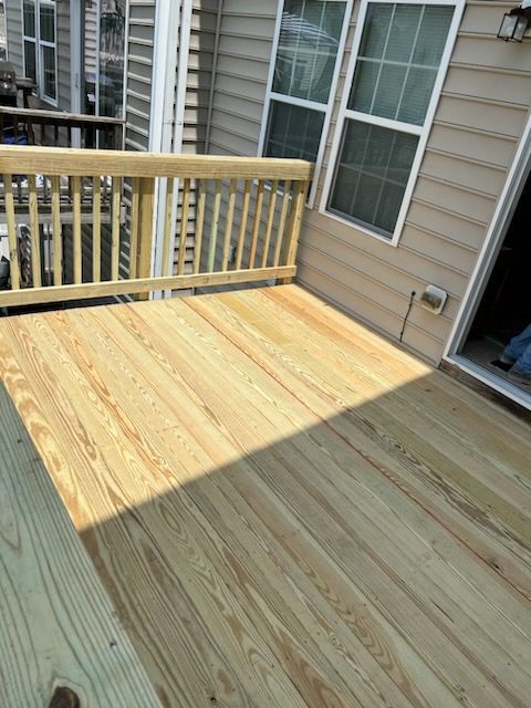 Newly built wooden deck with a railing against a beige house with windows.