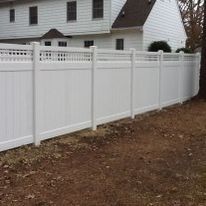 White vinyl fence in front of a white house on a brown, grassy yard.