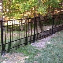 Black metal fence in a grassy yard, with trees in the background.