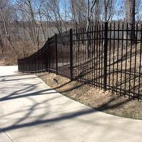 Black metal fence curves along a sidewalk. Sunlight casts shadows on the concrete.
