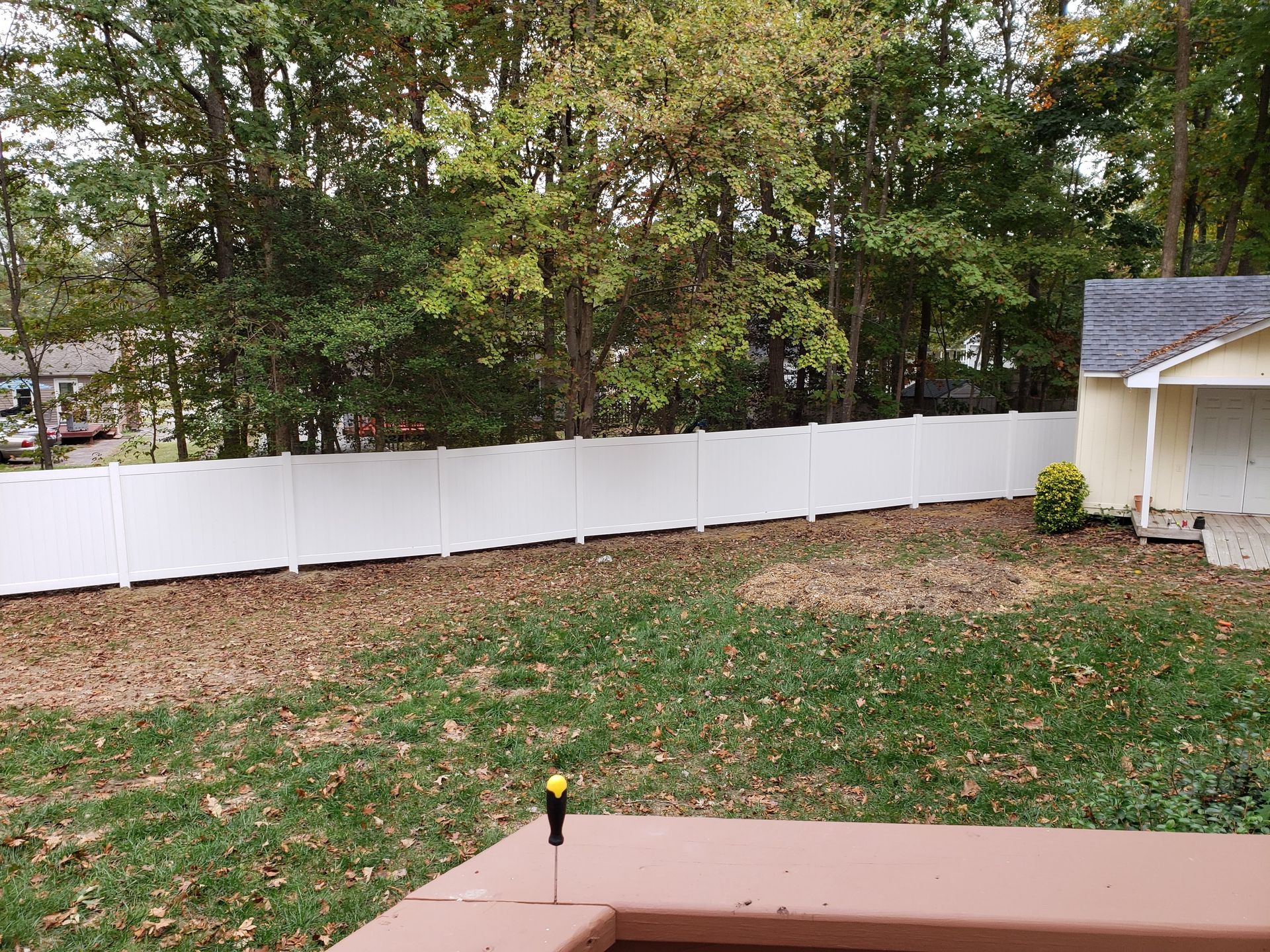 White fence bordering a backyard with trees in the background and a shed on the right.