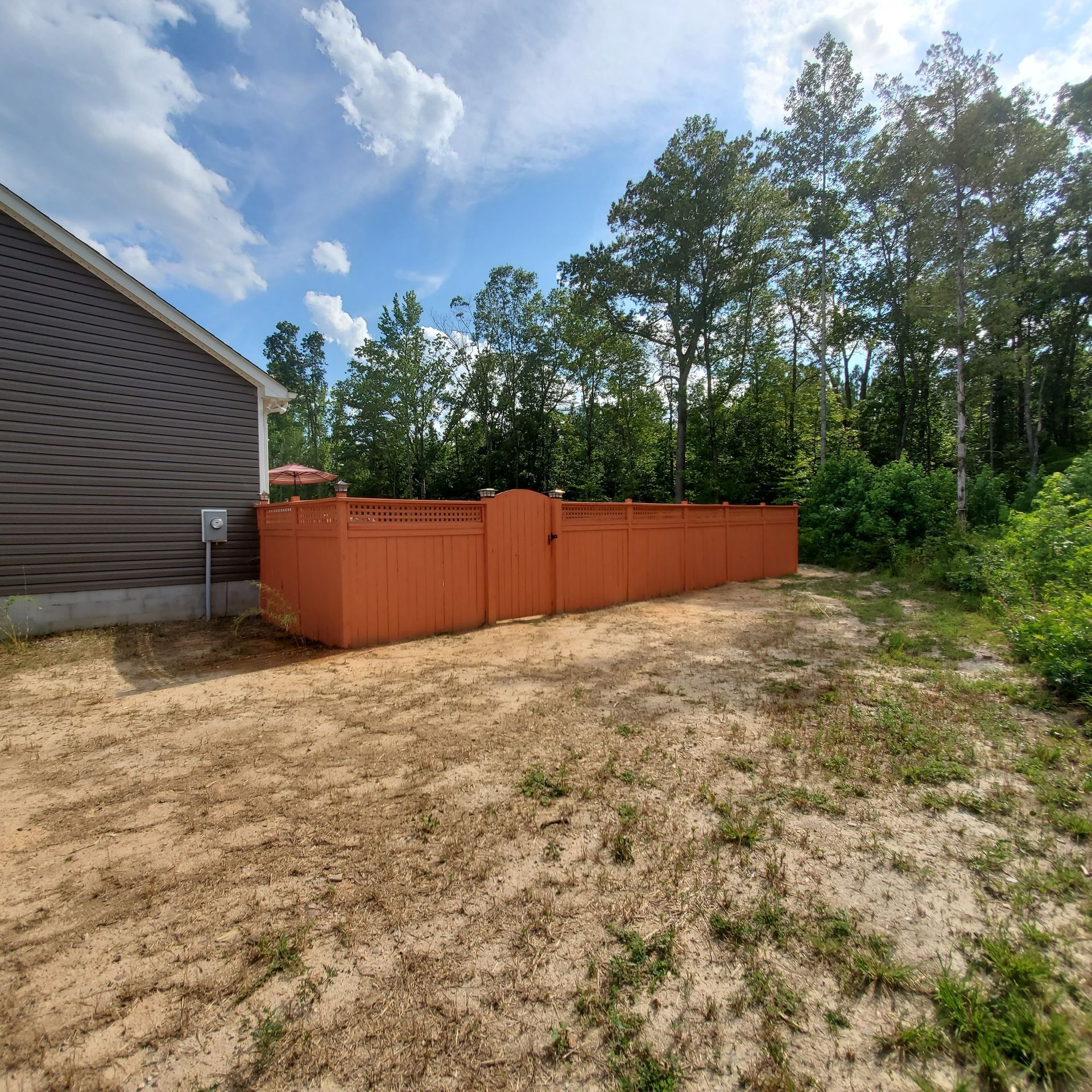 Orange fence encloses backyard, next to a house with trees in the background. Sunny day.
