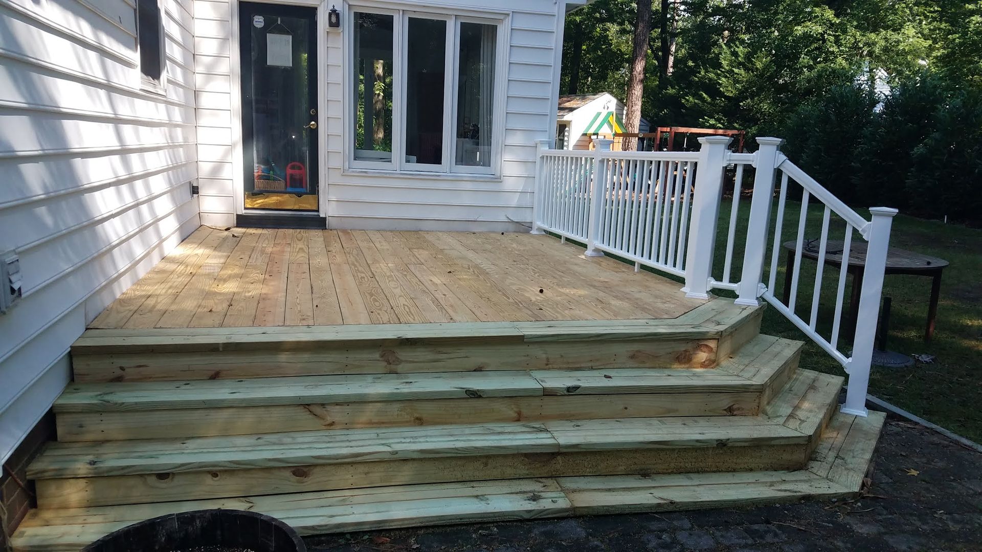 Wooden deck with white railing and steps leading down from a house.