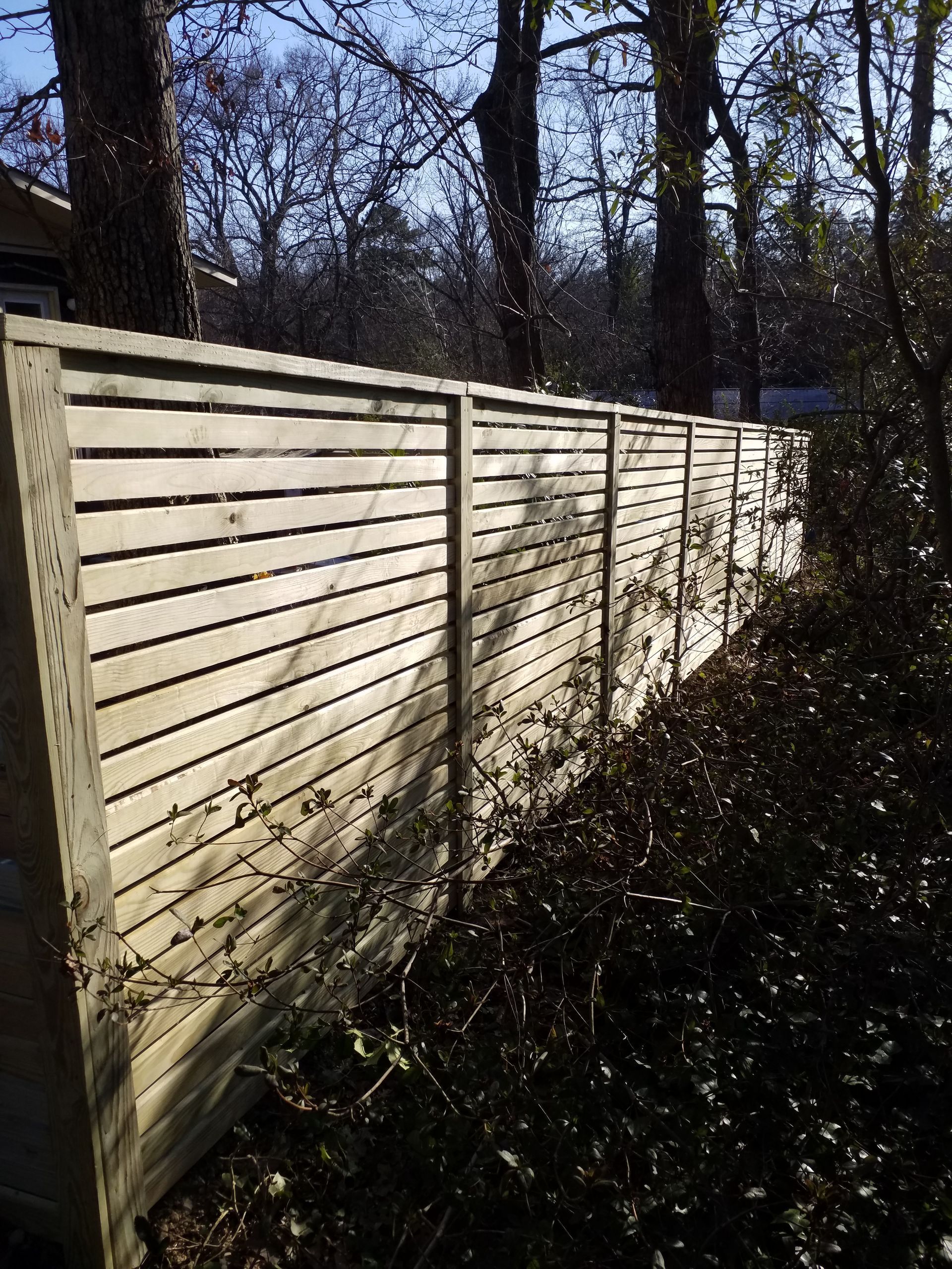 Wooden fence with horizontal slats in a sunny outdoor setting, with trees in the background.