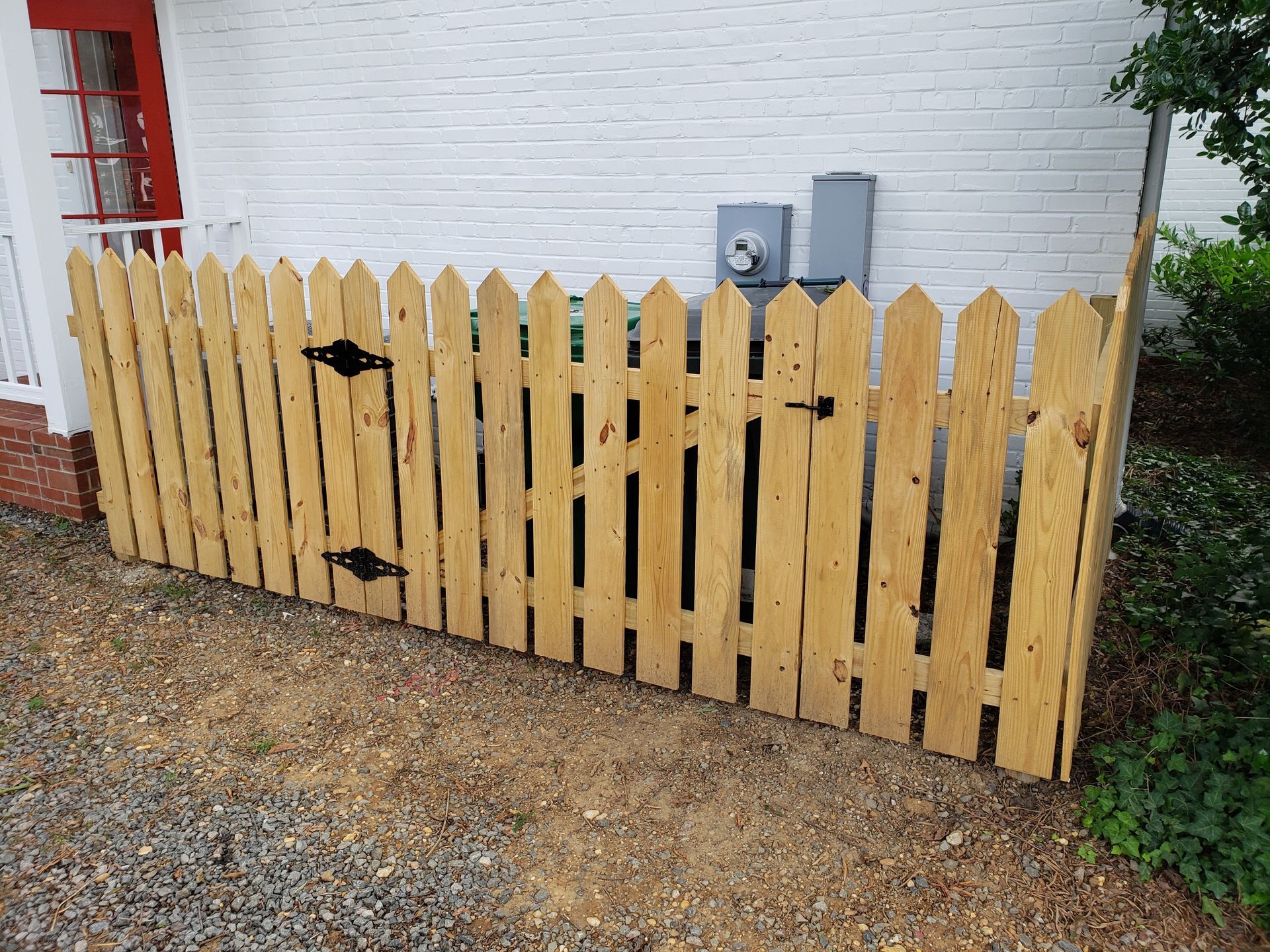 Wooden picket fence next to a white brick wall, concealing utility equipment.