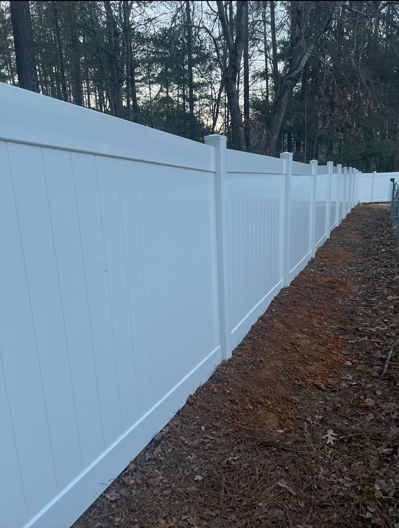 White vinyl fence in a wooded area.