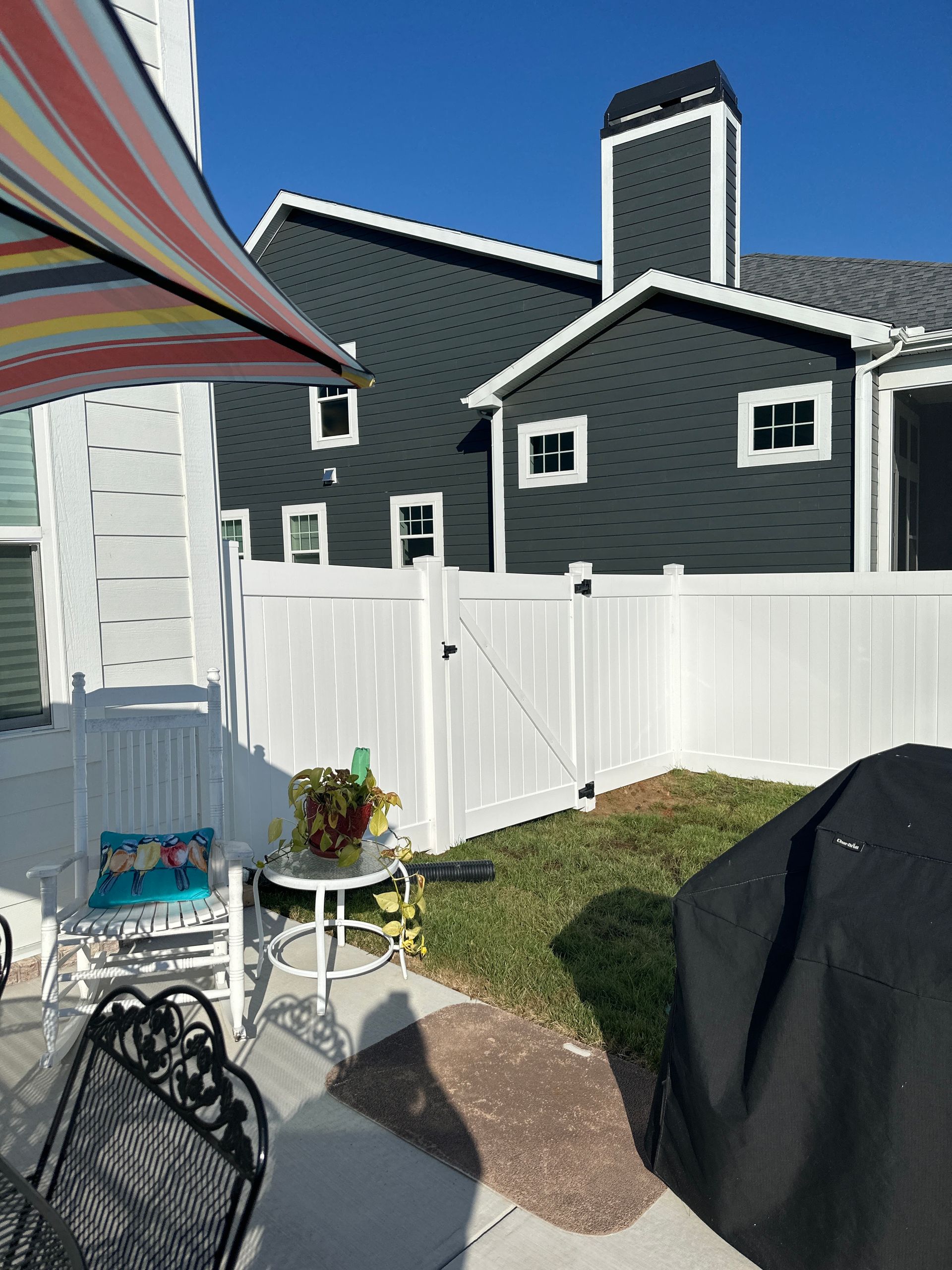 Backyard scene with white fence, patio furniture, and dark gray house in the background.