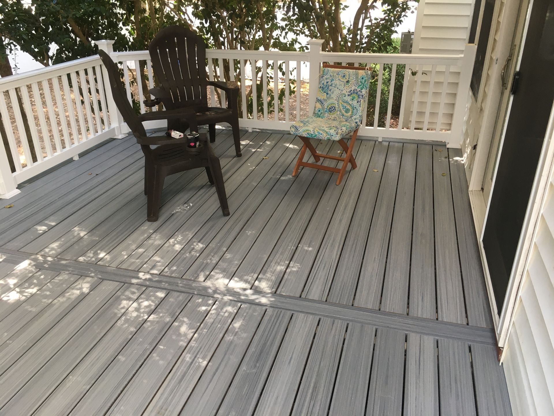 Grey deck with two brown chairs and a folding chair with a blue cushion; white railing.
